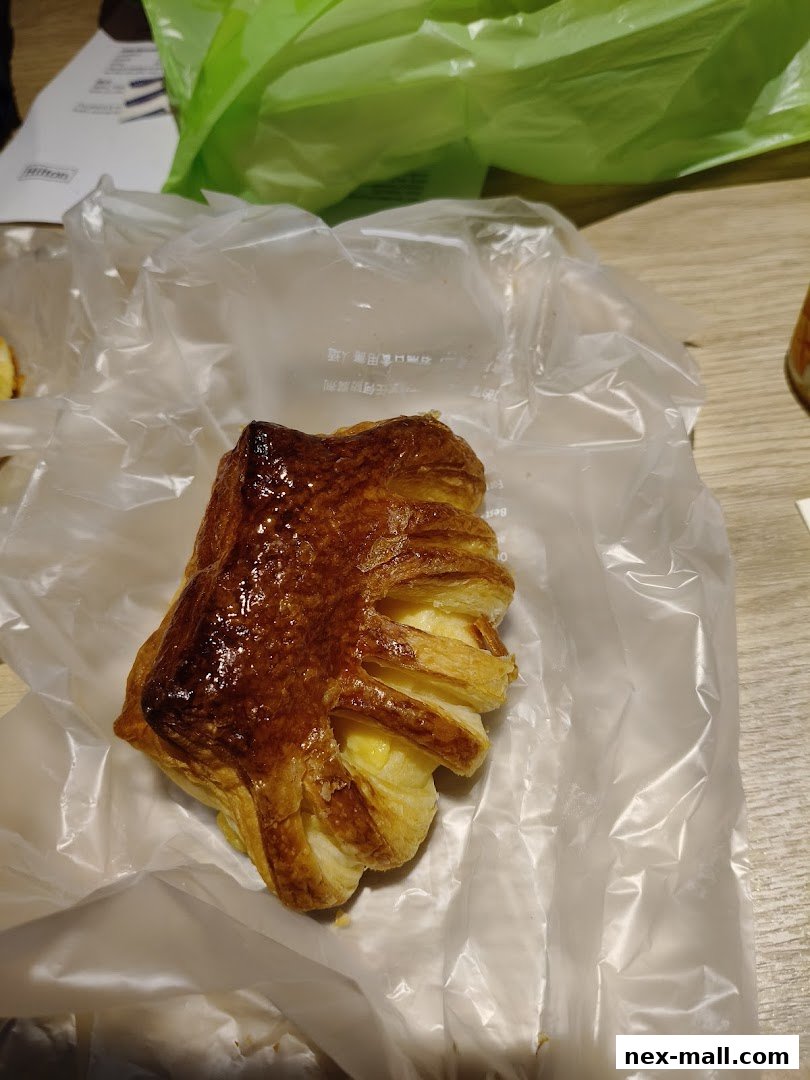 A golden-brown pastry with flaky layers and a creamy filling, presented in plastic packaging.