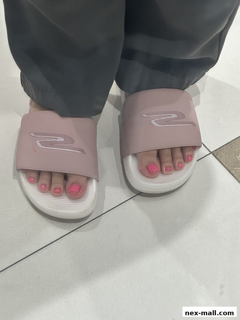 A person's feet wearing pink slides with bright pink toenails.