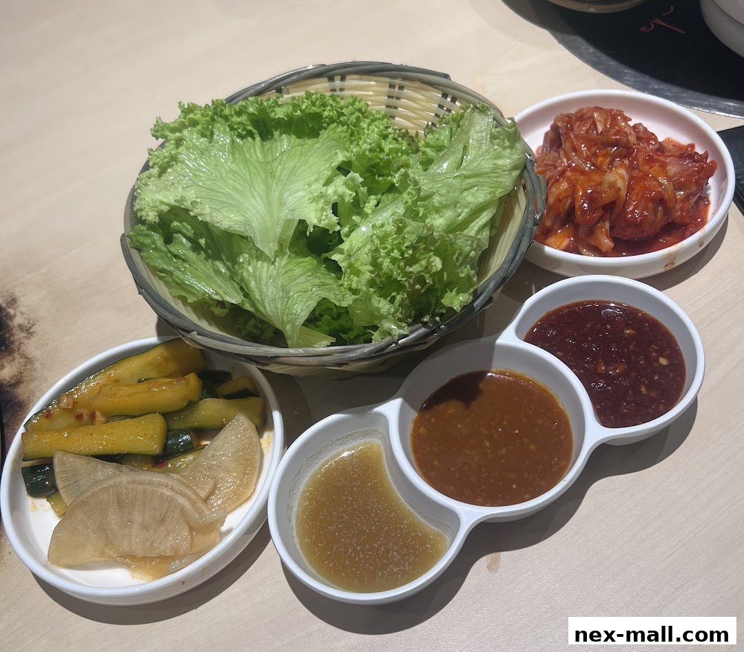 A selection of Korean side dishes including lettuce, kimchi, pickled cucumbers, and dipping sauces.