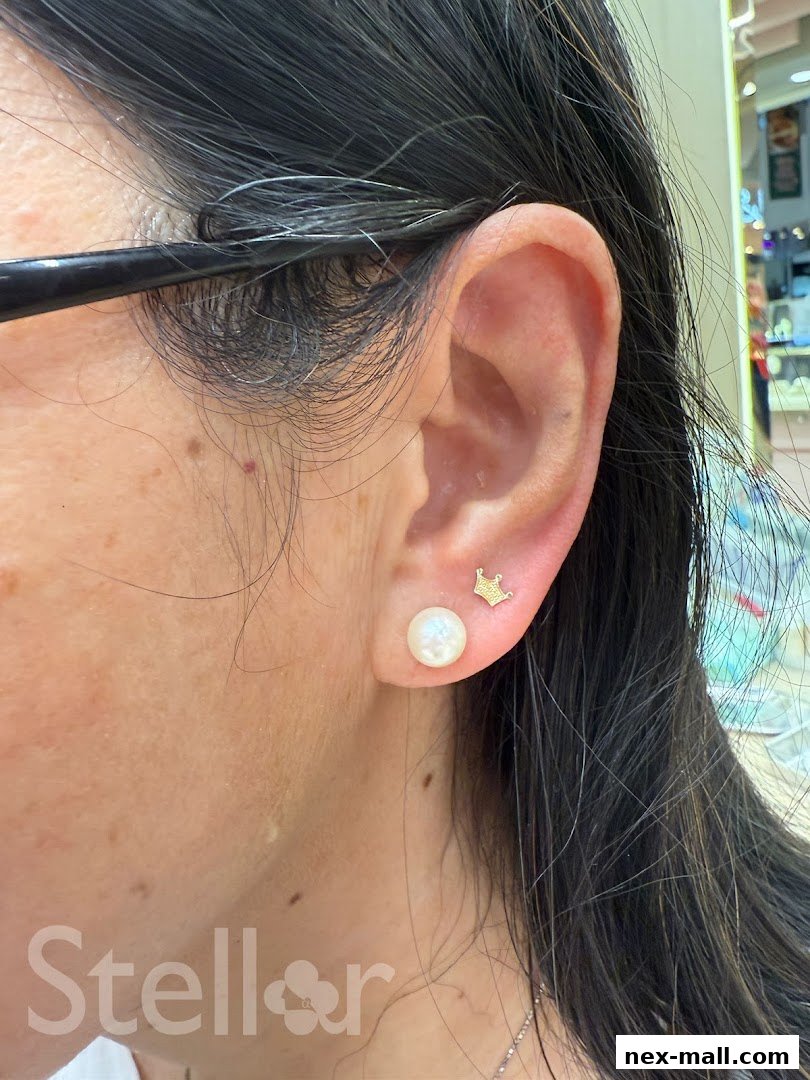 Close-up of a woman's ear adorned with a pearl stud and a small crown earring.
