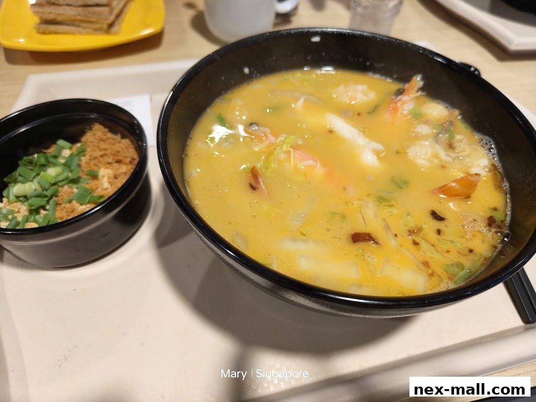 A close-up of a steaming bowl of soup with shrimp and vegetables, served with a side dish.