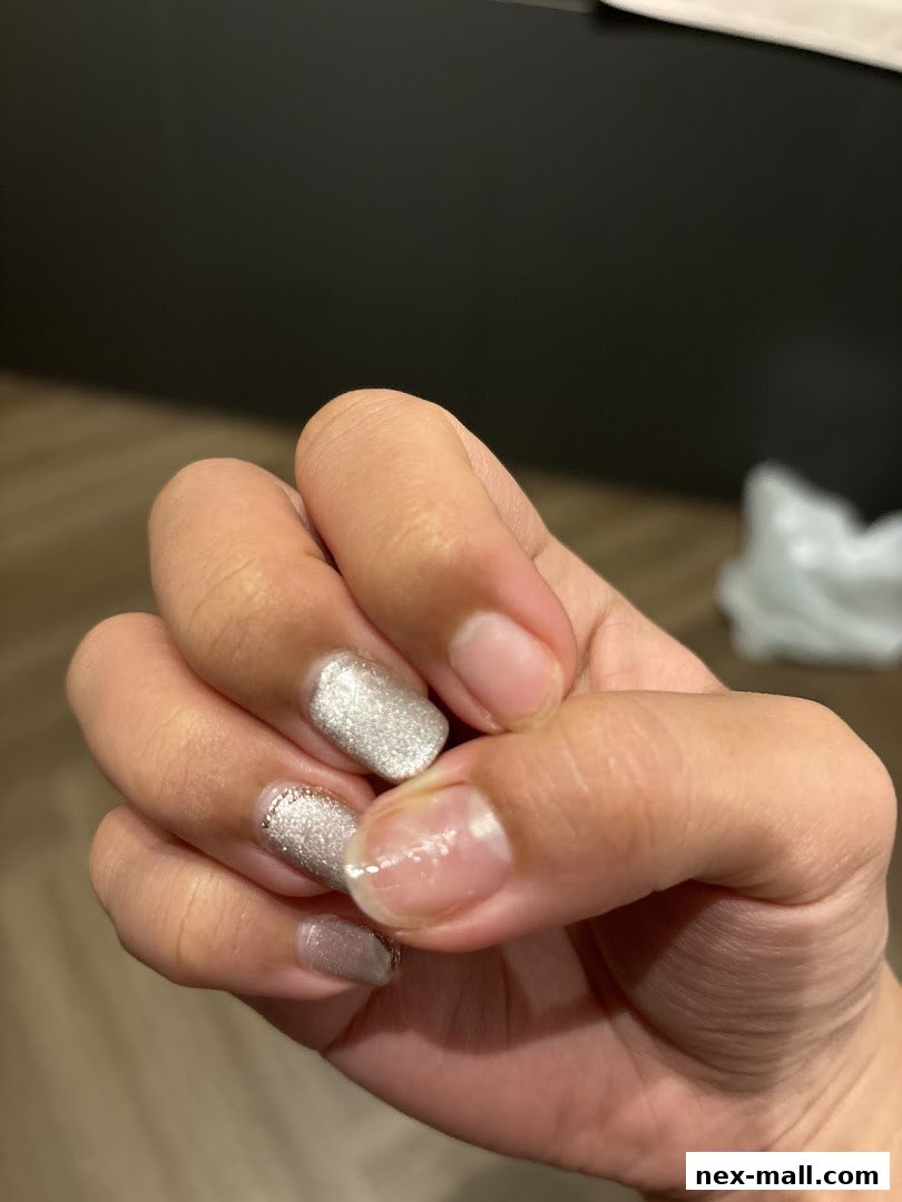 A close-up shot of a hand with partially done silver glitter nail polish.