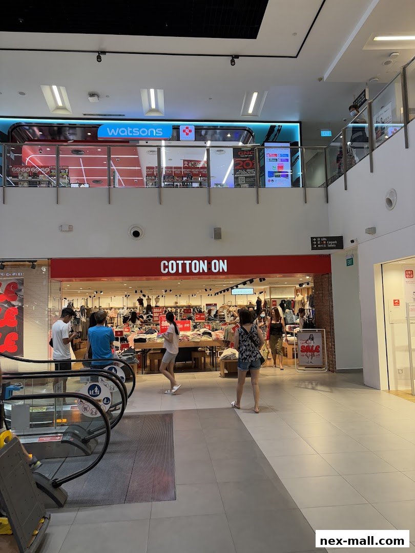 The Cotton On store entrance with shoppers browsing inside and an escalator in the foreground.