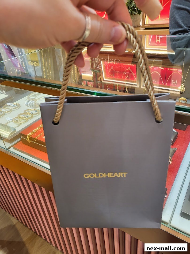 A hand holds a Goldheart jewelry shopping bag in front of a display case.