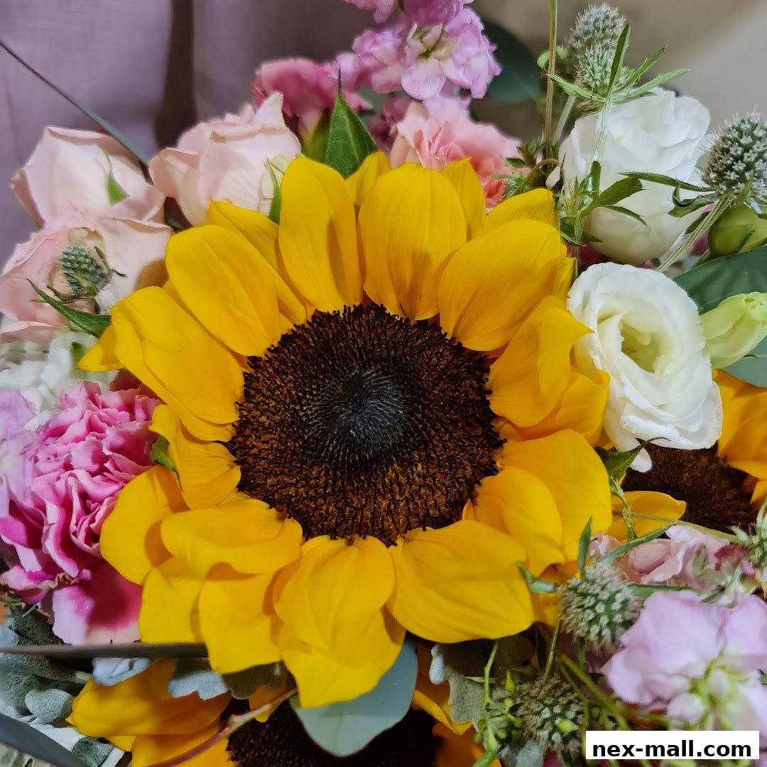 A vibrant bouquet featuring a large sunflower surrounded by pink roses, carnations, and white lisianthus.