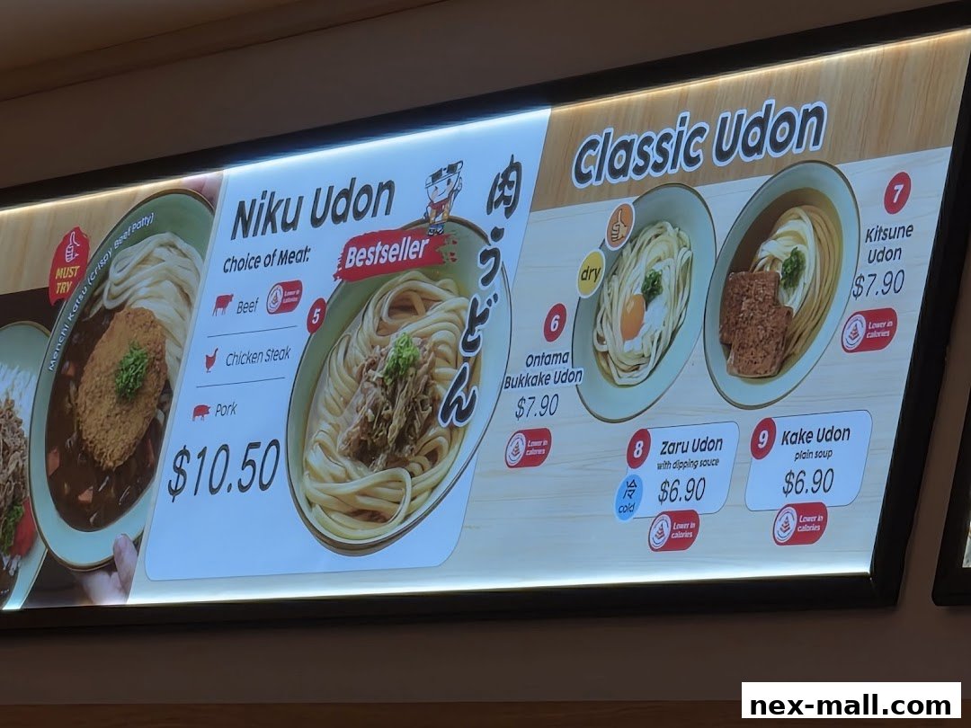 A brightly lit menu board displaying various udon dishes with prices and descriptions.