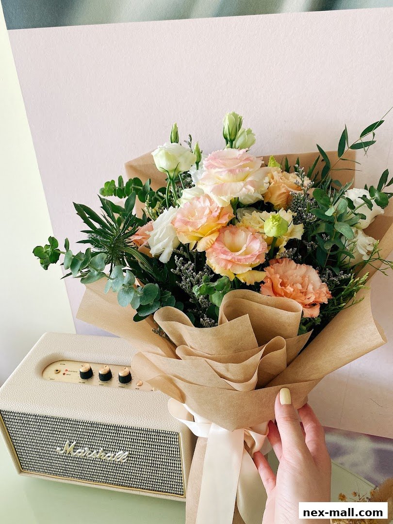 A hand holding a beautifully arranged bouquet of pastel-colored flowers next to a vintage speaker.