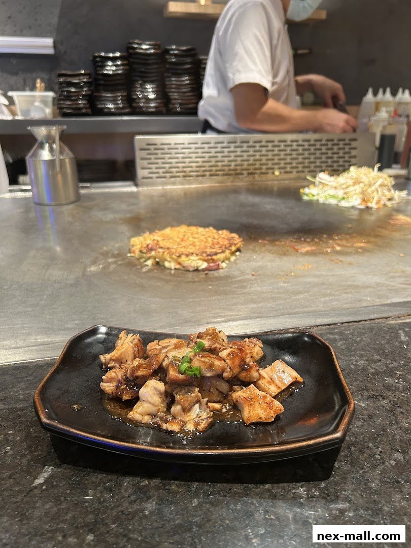 A plate of grilled chicken teriyaki is served in front of a teppanyaki grill with a chef preparing food.
