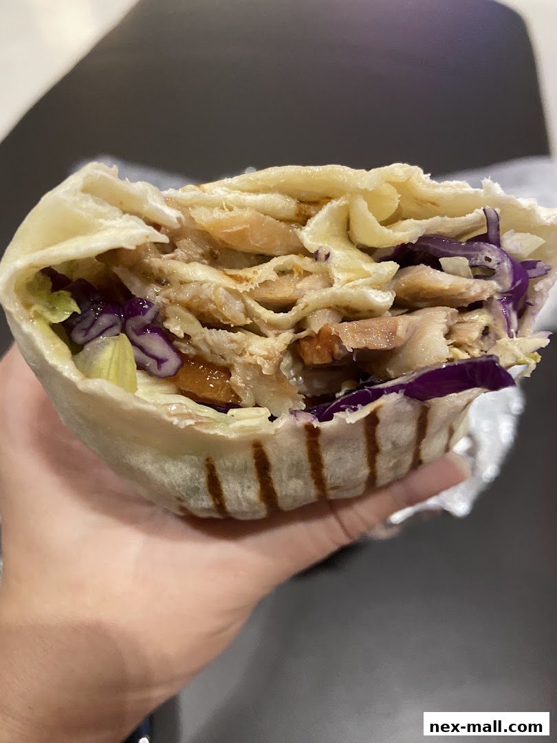 A hand holds a delicious-looking wrap filled with chicken, cabbage, and lettuce.