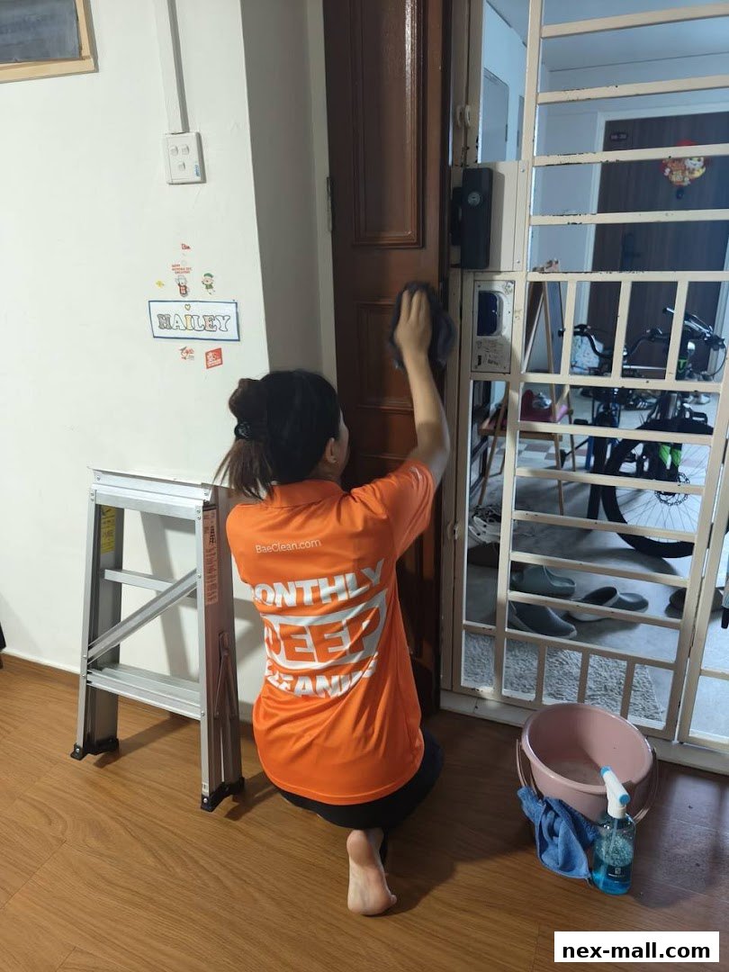 A person in an orange shirt cleans a door with a cloth, with cleaning supplies nearby.