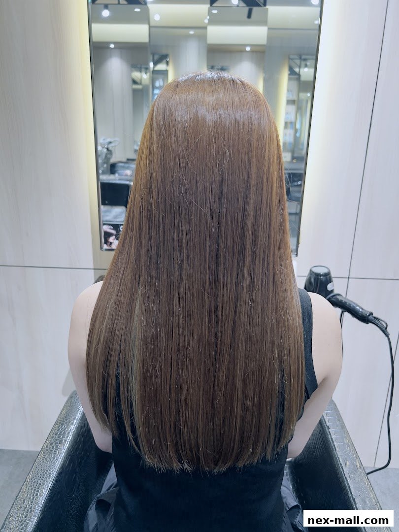A person with long, straight, brown hair sitting in a salon chair, viewed from behind.
