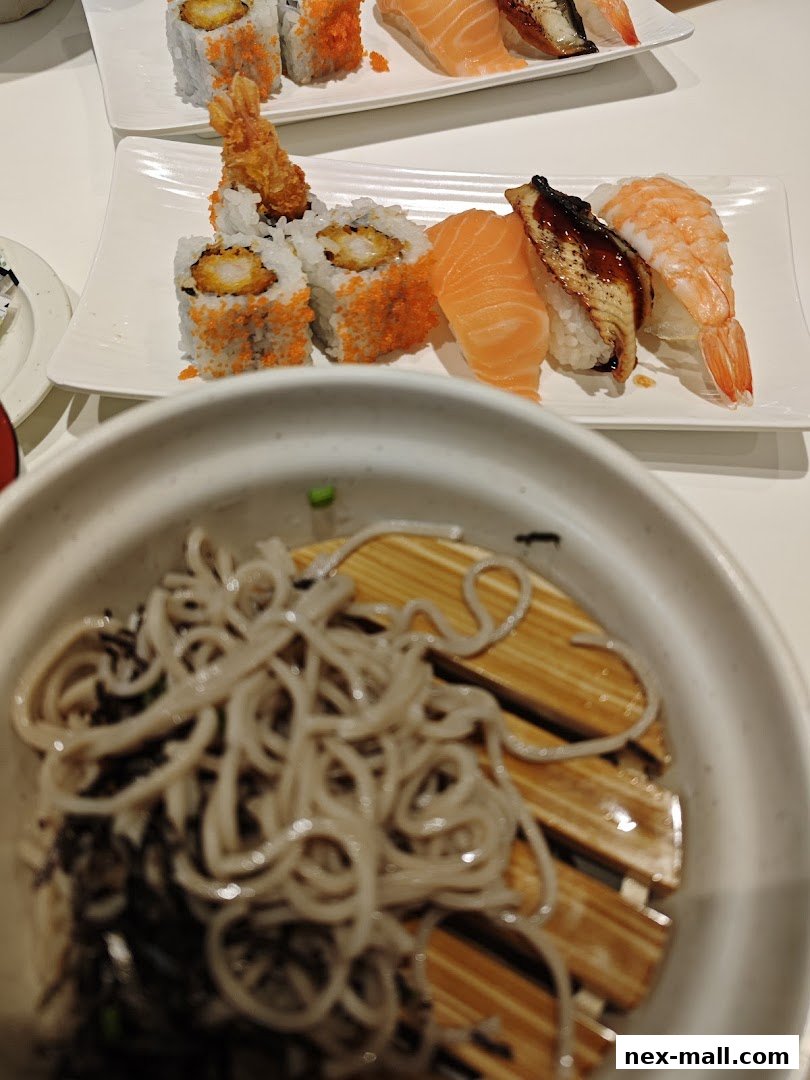 Plates of sushi and a bowl of soba noodles are displayed on a white table.