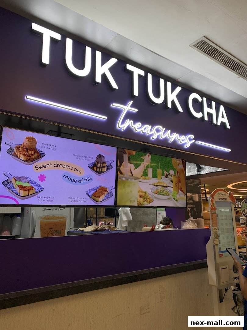 The storefront of Tuk Tuk Cha Treasures NEX, featuring illuminated signage and digital displays of food items.