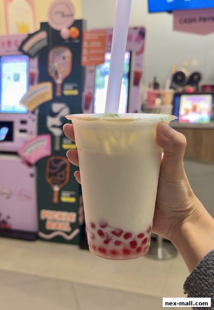 A hand holds a cup of bubble tea with red pearls at the bottom.