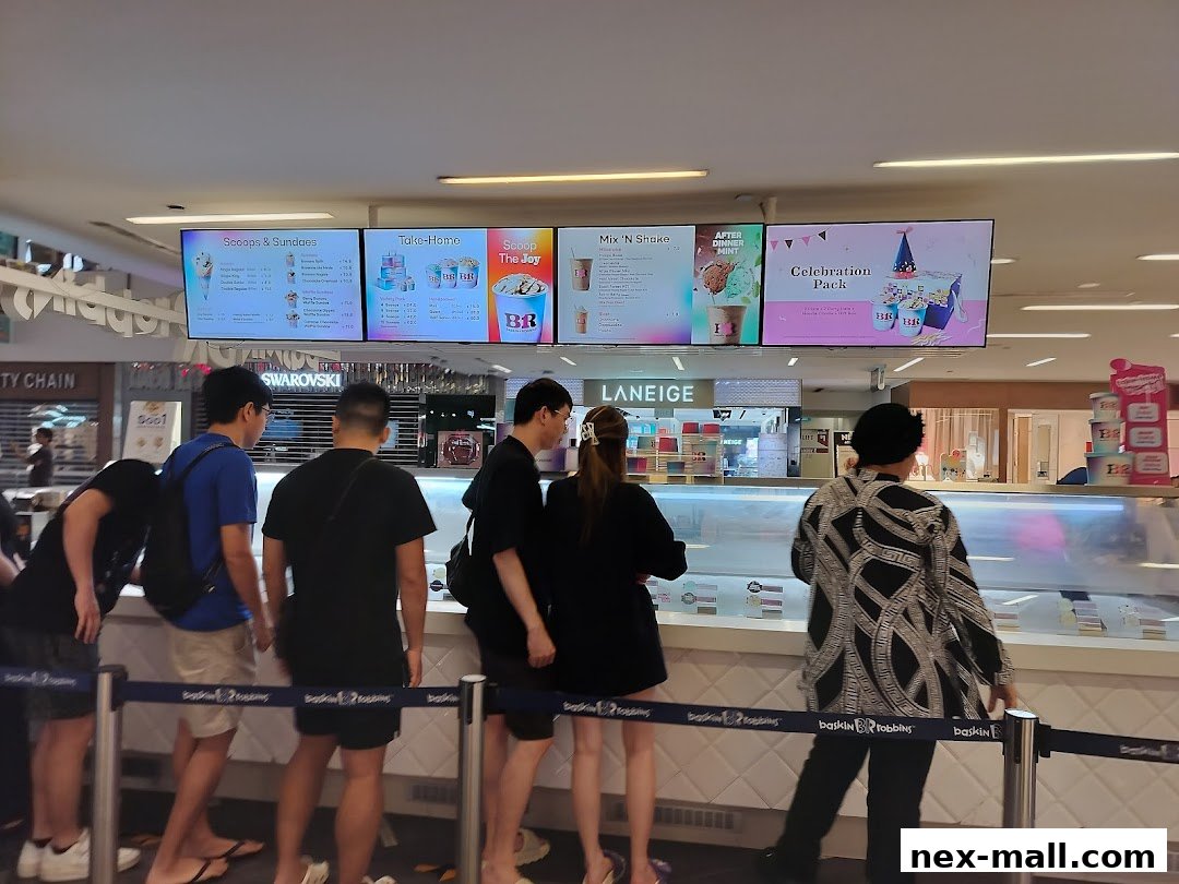 People queuing at a Baskin Robbins ice cream shop with digital menus displaying products.