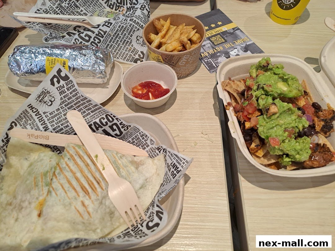 A table laden with Mexican food including a burrito, nachos, fries, and a small cup of sauce.