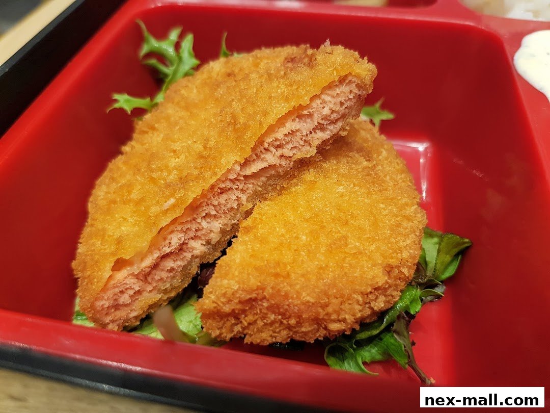 A close-up of a golden-brown fried cutlet, sliced in half, served with lettuce in a red container.