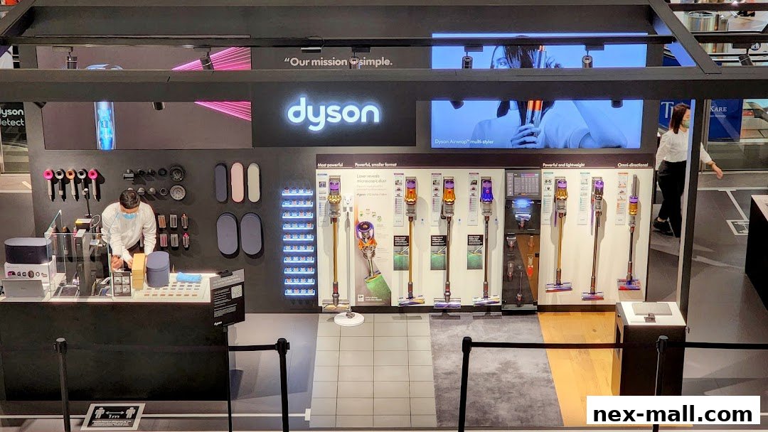 A Dyson store display featuring vacuum cleaners, hair stylers, and accessories with a staff member at the counter.