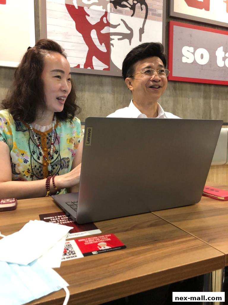 Two people are looking at a laptop on a wooden table, with KFC branding in the background.