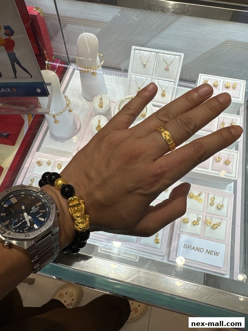 A person's hand wearing a gold ring and a beaded bracelet displays jewelry in a display case.