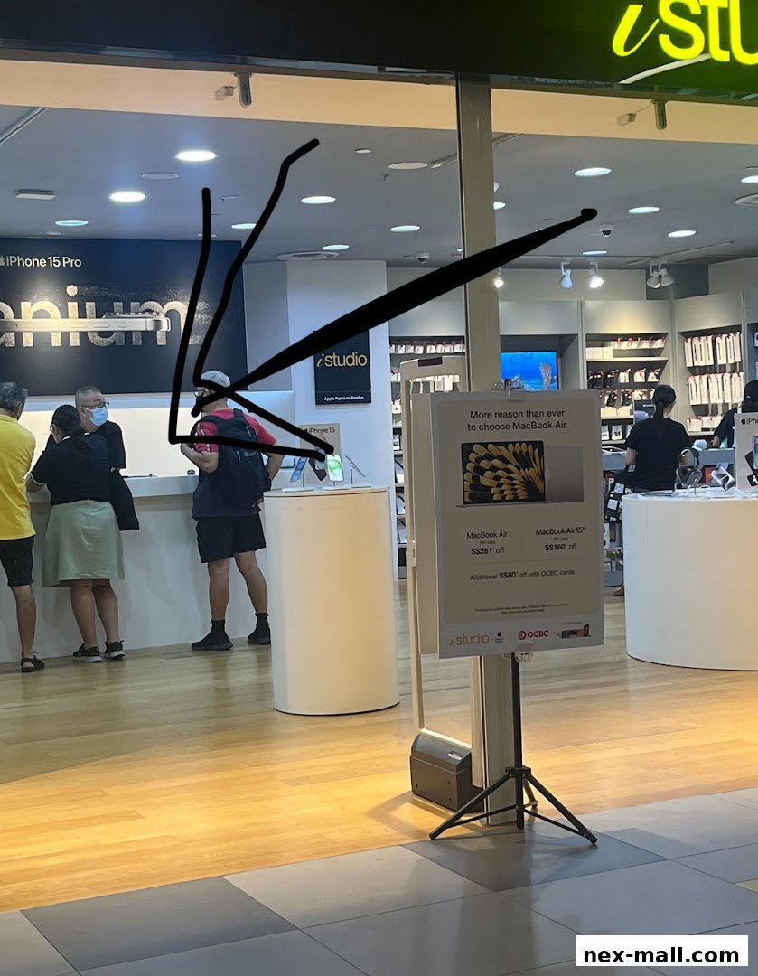 Customers browse Apple products at the iStudio NEX store, with promotions displayed.
