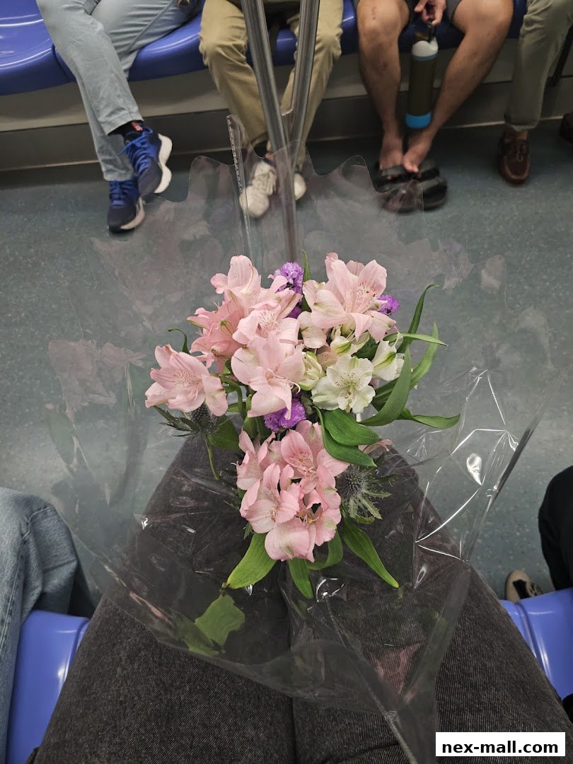 A bouquet of pink and white flowers is held by a person sitting on a public transport seat.