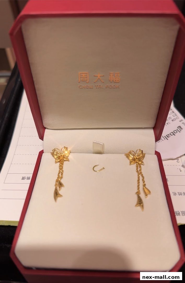 A pair of gold butterfly earrings with dangling charms in a red jewelry box.