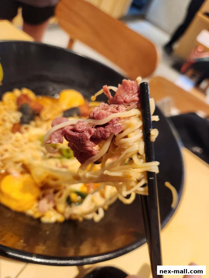Close-up of a person holding chopsticks with noodles and beef from a bowl of Mala Tang.