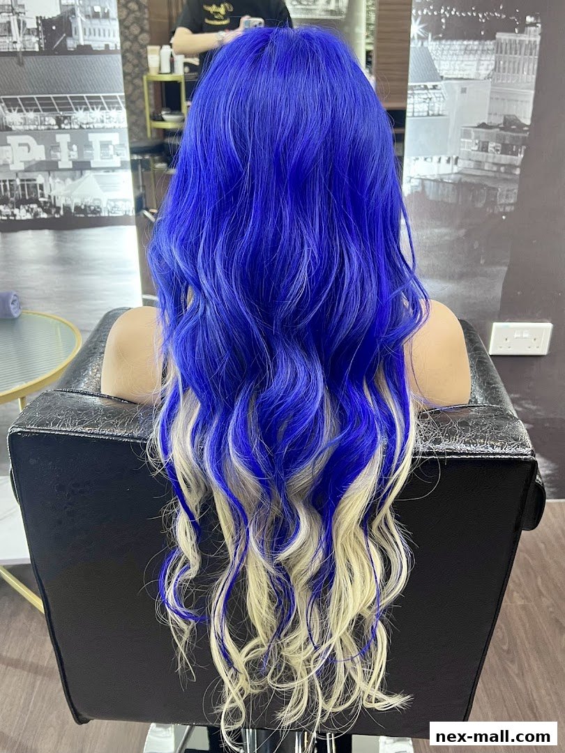 A person with vibrant blue and blonde ombre hair styled in waves, seated in a salon chair.