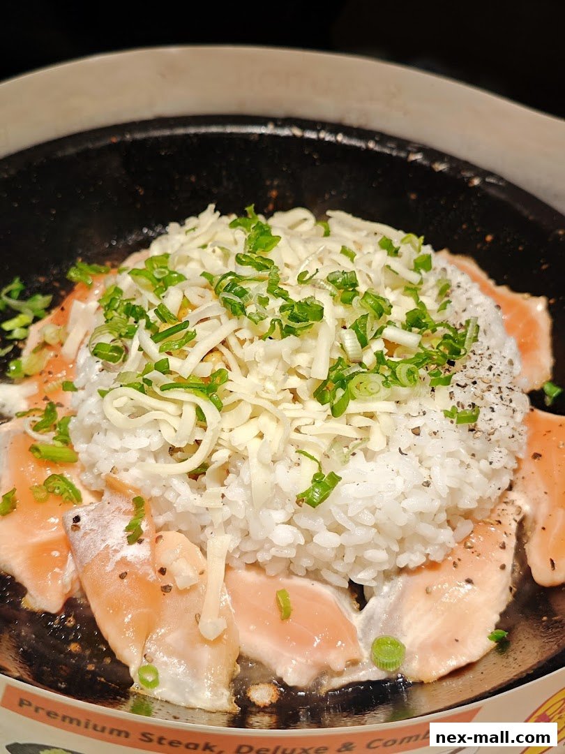 A close-up of a sizzling hot plate dish with salmon, rice, cheese, and green onions.