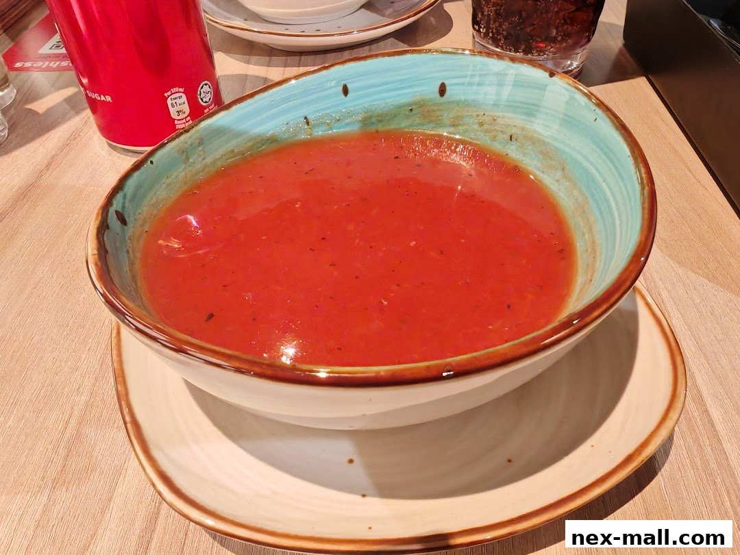 A bowl of hearty tomato soup served with a drink and a can.