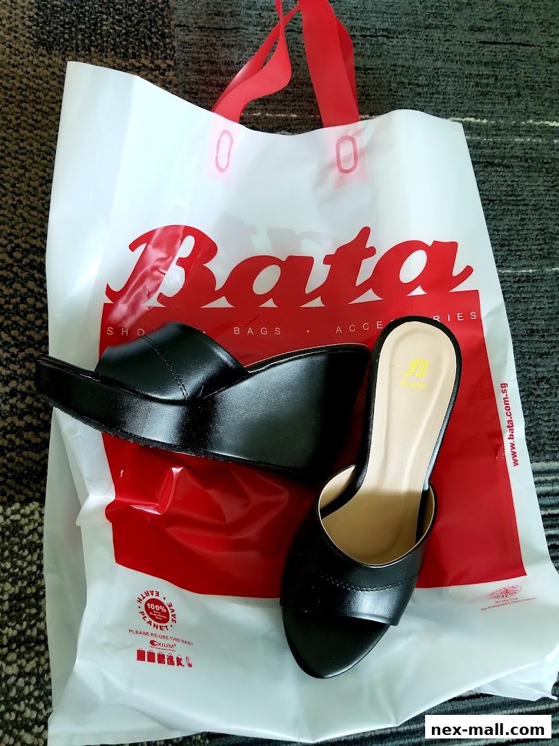 A pair of black wedge sandals displayed on a white Bata shopping bag.