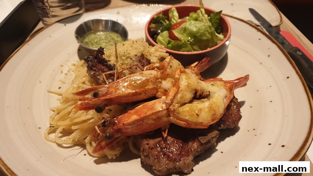 A plate of spaghetti with grilled prawns and steak, served with a side salad and dipping sauce.