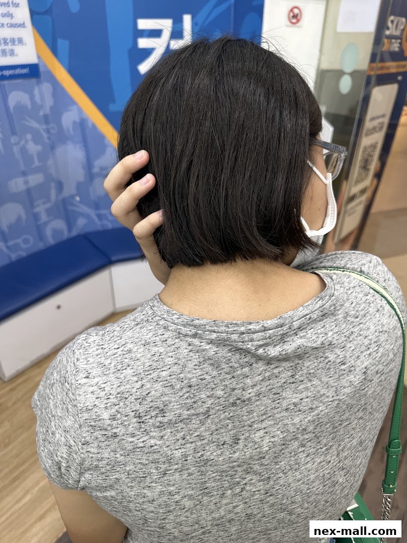 A person with short dark hair and glasses is seen from behind, touching their hair.