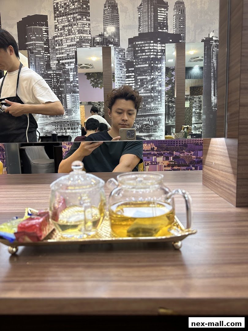 A man takes a selfie in a salon with a tray of tea and sweets in the foreground.