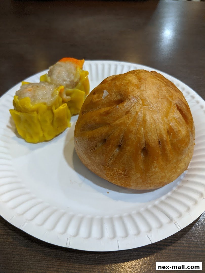 A plate of dim sum, featuring two siu mai and a baked bun.