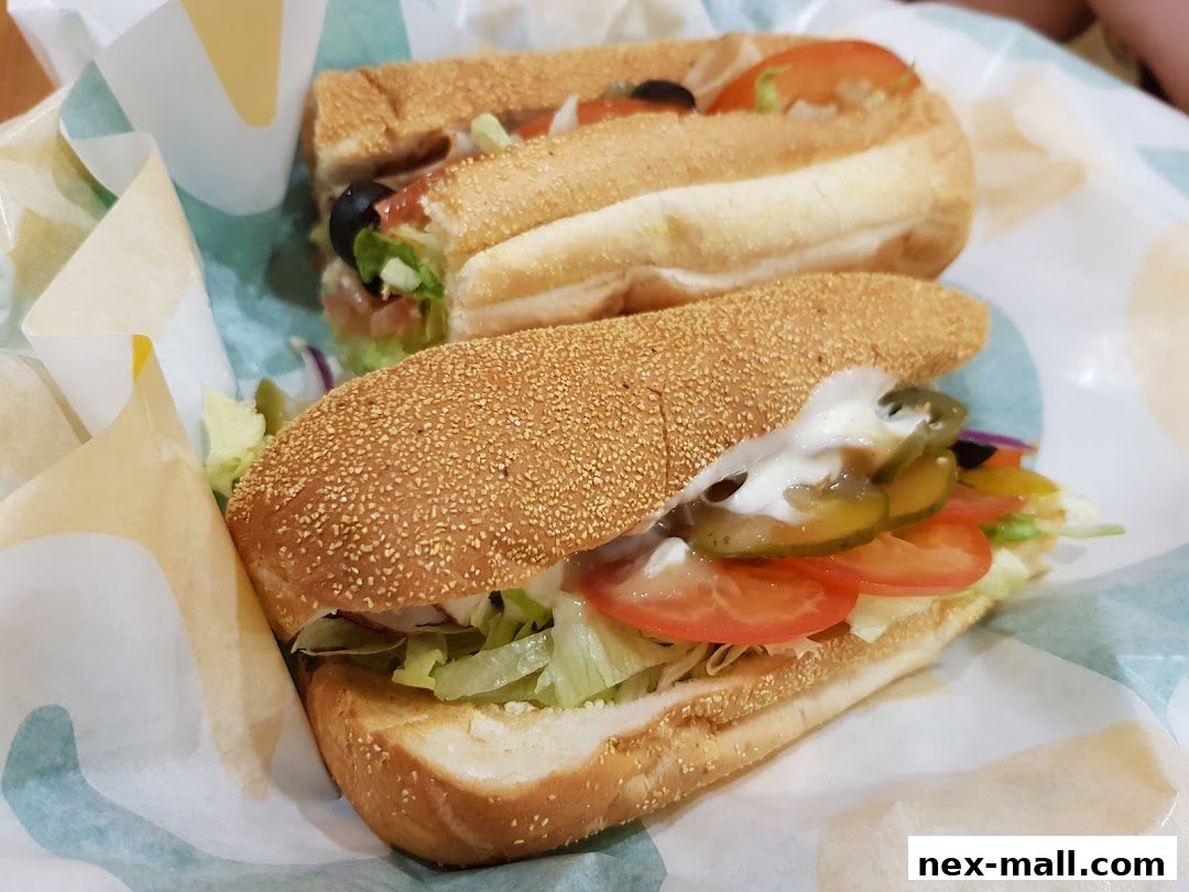 Two freshly made Subway sandwiches with various toppings and sauces.