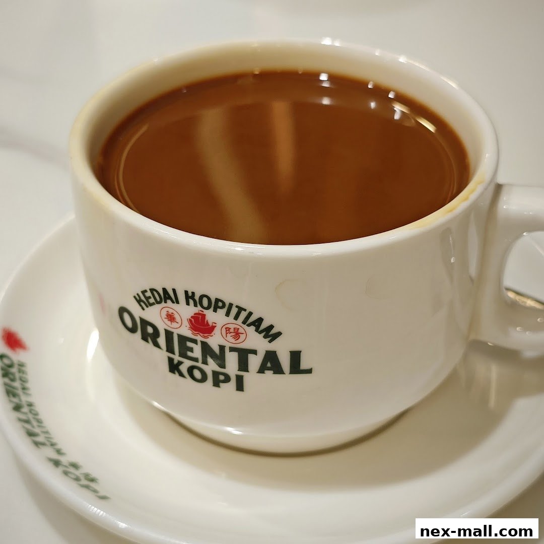 A close-up shot of a steaming cup of coffee with the Oriental Kopi logo on the mug.