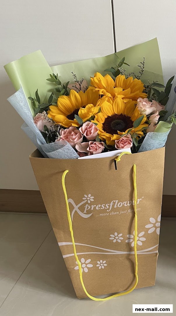A bouquet of sunflowers and pink roses in a branded paper bag.