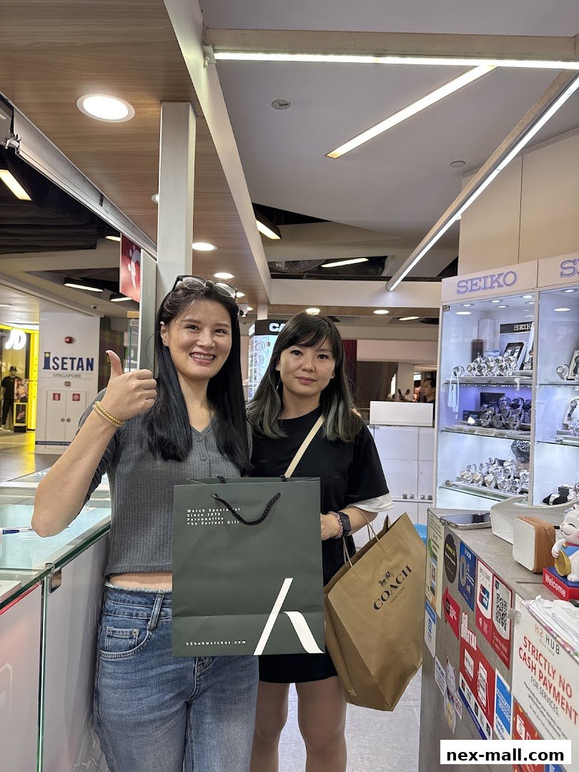 Two women posing with shopping bags in front of a watch store display.