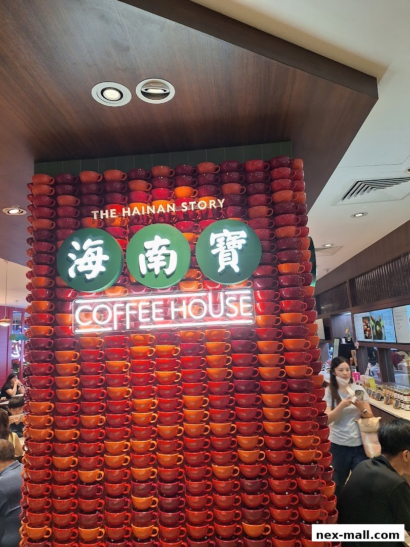 The Hainan Story Coffee House Nex features a striking wall display of stacked coffee cups.