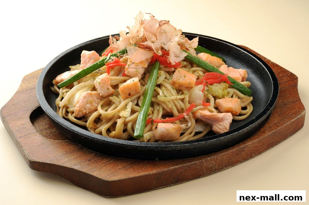 A sizzling plate of yakisoba with salmon, green onions, and bonito flakes.