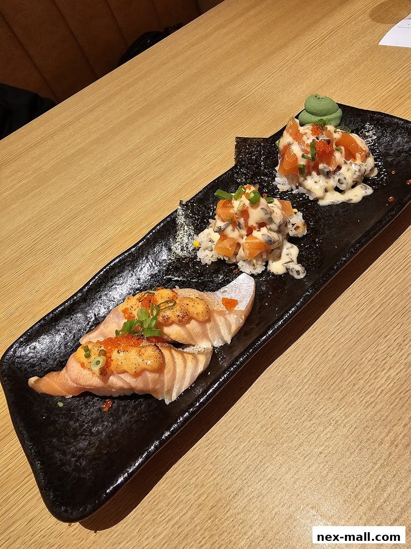 A black platter holds three servings of sushi with salmon and creamy toppings.