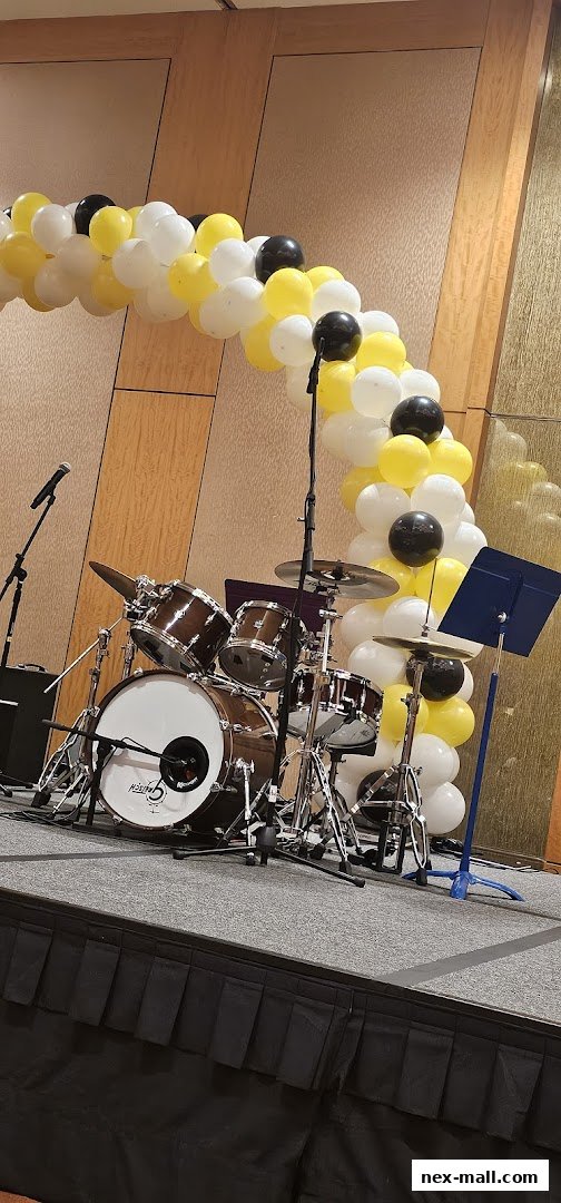 A drum set on a stage decorated with a balloon arch and microphones.