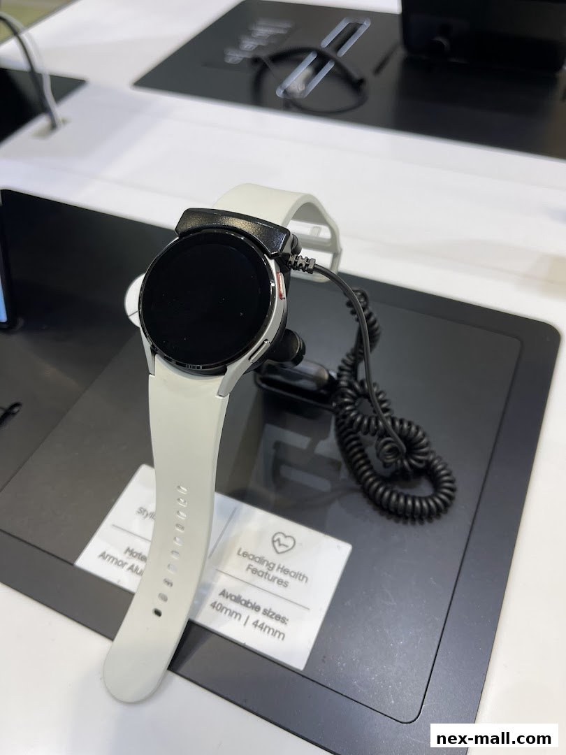 A white Samsung smartwatch with a black screen is displayed on a stand.