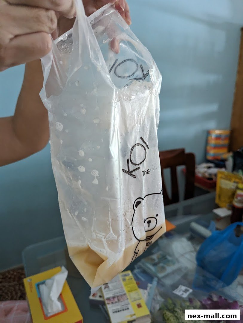 A person holds a plastic bag with the KOI Thé logo and a bear illustration, containing a drink.