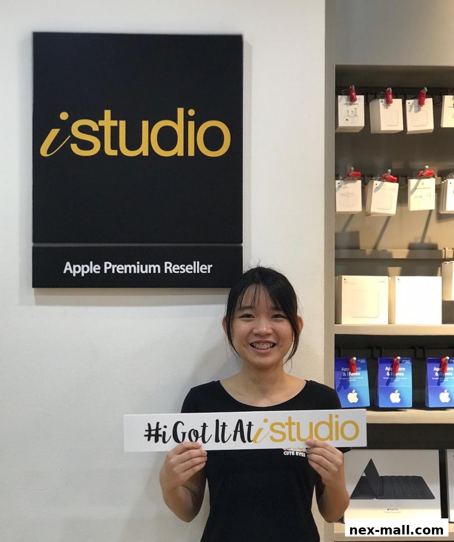 A young woman smiles holding a sign that says '#iGotItAt iStudio' in front of an Apple Premium Reseller store.