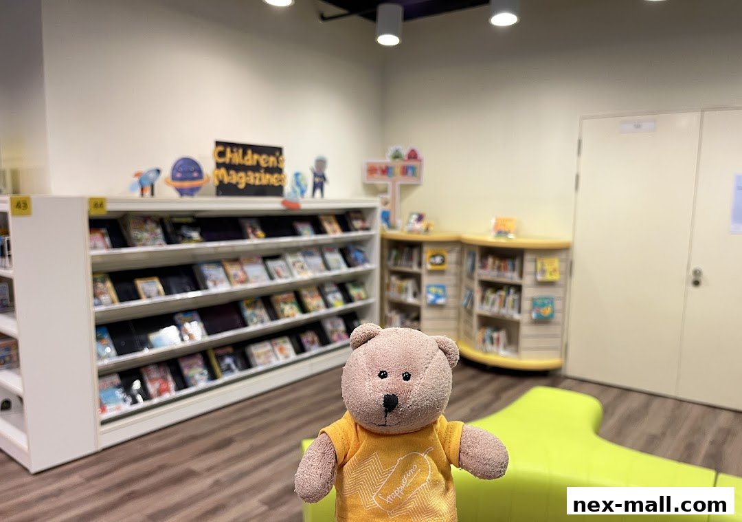 A teddy bear stands in front of shelves filled with children's magazines and books at a library.