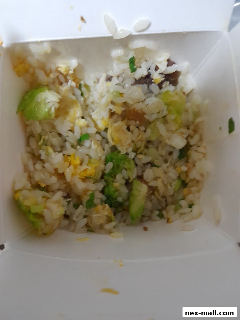 A close-up shot of a takeaway box filled with fried rice, vegetables, and egg.