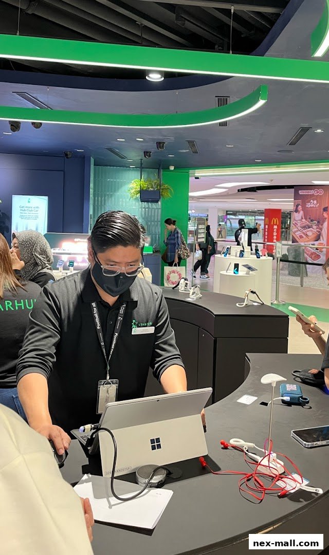 A StarHub store employee assists a customer at a counter with a laptop and display of mobile phones.